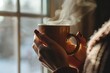 closeup of hands holding a warm mug, steaming near window