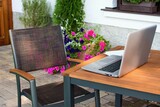 Fototapeta Do akwarium - Home working place with laptop in the beautiful summer terrace and blooming garden