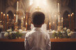 Young boy of African descent in a white suit positioned at the church altar with candles and a crucifix. Back shot attending a religious service or ceremony. First communion concept.