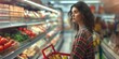A stunning young woman at the supermarket looks through the canned goods section of the store. Her shopping basket is brimming with wholesome food items.