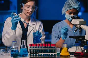 Life scientists researching in laboratory. Focused female life science professional pipetting solution into the glass cuvette. Healthcare and biotechnology concept.