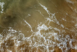Fototapeta Boho - Foamy sea wave on the sandy shore. Muddy dirty green water surface. Top view. Background. Space for text.