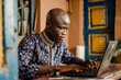 handsome african man using laptop while sitting at table in cafe

