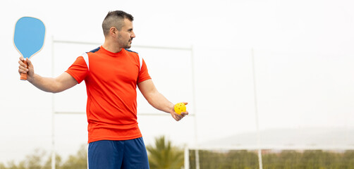 A grown man in sportswear is playing a game of pickleball.The young man is about to serve the ball in the game.Copyspace for advertising.Pickle ball.