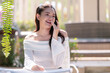 © Wasana - A cheerful young woman with a playful smile sits at a casual outdoor cafe table. with bright sunlight