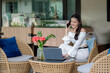 © Wasana - A young woman talking on the phone while working on a laptop in a quiet outdoor cafe.