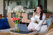 © Wasana - A young woman talking on the phone while working on a laptop in a quiet outdoor cafe.
