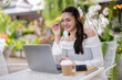 © Wasana - Young woman enjoying a video call using a laptop at an outdoor cafe. Enjoy chatting on laptop screen.
