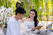 © Wasana - Two colleagues share a light-hearted moment while discussing work, with a laptop, in a verdant outdoor café setting.