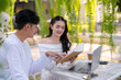 © Wasana - Two colleagues share a light-hearted moment while discussing work, with a laptop, in a verdant outdoor café setting.