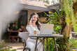 © Wasana - A young woman talking on the phone while working on a laptop in a quiet outdoor cafe.