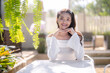 © Wasana - A cheerful young woman with a playful smile sits at a casual outdoor cafe table. with bright sunlight