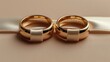  Two golden wedding rings on white satin ribbons on beige surfaces