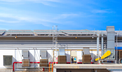 Exhaust duct and ventilation equipment in EVAP system on the wall with solar panels on steel roof of industrial building against blue sky background