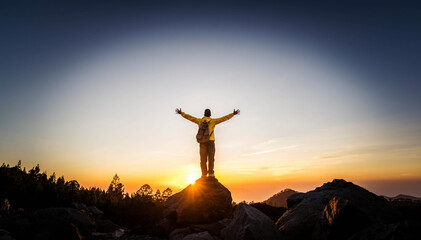 Wall Mural - Male hiker climbing the mountain - Strong hiker with hands up standing on the top of the cliff enjoying sunset view