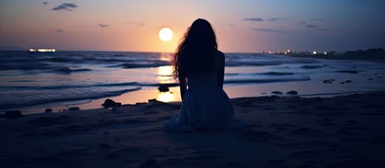 Aufkleber - A woman seated on the shore, observing the sun as it sets over the horizon