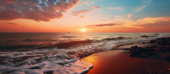 Aufkleber - Scenic view of the sun setting on the horizon where a river flows into the sea, with waves gently crashing on the shore