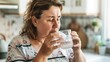 © iuricazac - Woman with curly hair wearing a floral top drinking water from a glass in a kitchen.