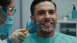 Cropped portrait of handsome man with braces sitting in dental chair. Doctor in gloves holding examination tools behind. Braces, alignment of teeth.