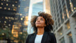 Portrait of beautiful young black businesswoman with curly hair in the city looking up at skyscrapers.