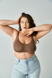 Fototapeta Nowy Jork - attractive plus size young woman in brown bra and blue jeans looking to side and posing with hands