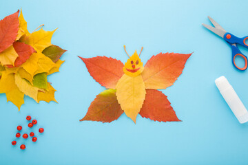 Wall Mural - Created butterfly shape from colorful leaves on light blue table background. Pastel color. Making autumn decorations. Closeup. Top down view.