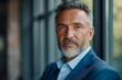 Close-up portrait of elegant, stylish mature businessman with trimmed beard in formal wear. Perfectly fitted blue suit, light blue shirt with upper button undone. Senior executive in business attire.
