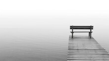 An Empty Wooden Bench On A Foggy Lake Pier, Evoking Feelings Of Solitude And Reflection