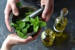 hands holding a mortar and pestle with fresh mint leaves, oil bottle beside