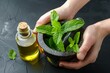 hands holding a mortar and pestle with fresh mint leaves, oil bottle beside