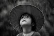 child with oversized hat looking up at rain