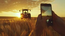 A farmer takes a photo of a working tractor on his field with a smartphone. In the heart of the field, the farmer captures the power of his trusty tractor on his smartphone.