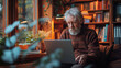A contemplative elderly man with a full beard is deeply engrossed in using a laptop in his warm, book-filled study, with plants adding a touch of nature.