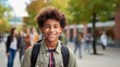 Photo of a glad, smiling young male student. Boy with a backpack ready to start studying university international exchange program summer holidays outdoors with a group of students in the background