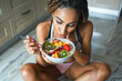 Shot of athletic woman eating a healthy bowl of muesli with fruit sitting on floor in the kitchen at home