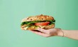 Hand holding a delicious fresh sandwich - A hand presenting a tasty sandwich with crispy bread, fresh lettuce, cheese, and tomato slices on a green background