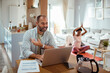 © Davor - Man working on laptop with woman in background doing yoga at home