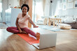 © Davor - Woman on yoga mat looking at laptop in living room