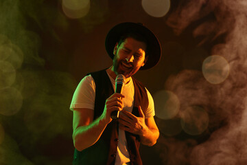 Handsome man with microphone singing on stage in color lighted smoke