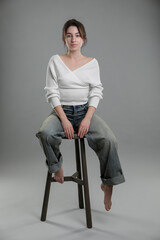 Sticker - Beautiful young woman sitting on stool against grey background