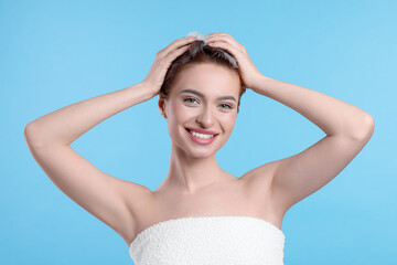 Wall Mural - Happy young woman washing her hair with shampoo on light blue background