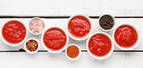 Wall Mural - Bowls with tasty tomato sauce and ingredients on white wooden background