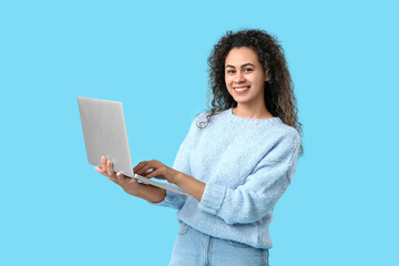 Young African-American woman with modern laptop on blue background