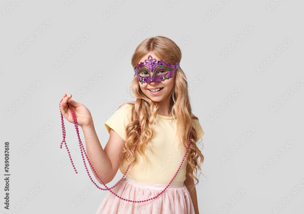Cute little girl wearing carnival mask on light background