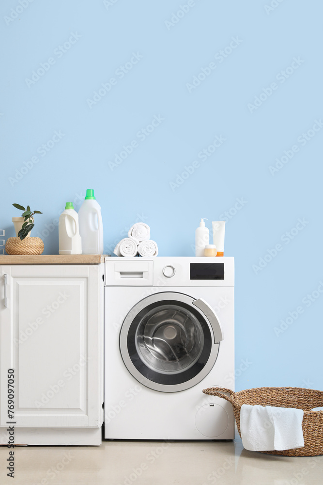 Modern washing machine with basket and cabinet near blue wall. Interior of home laundry room