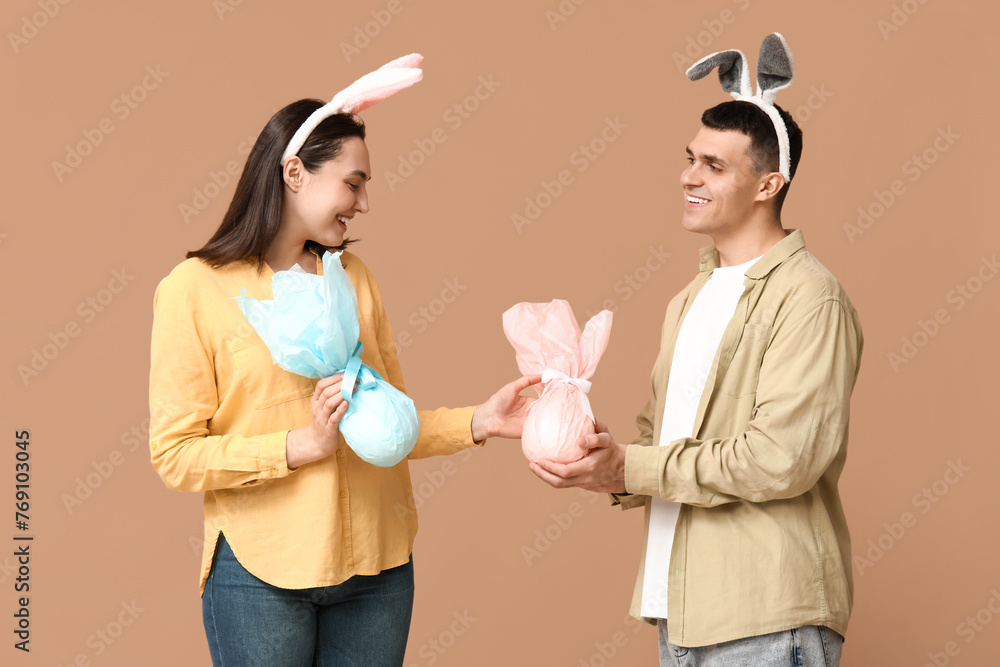 Happy young couple with Easter bunny ears and gifts on beige background