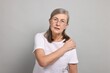 Arthritis symptoms. Woman suffering from pain in shoulder on gray background