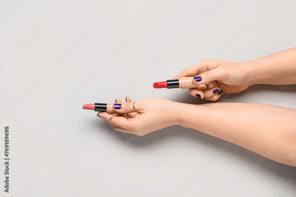 Female hands with lipsticks on grey background