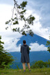 A young man stands with his back in a black raincoat enjoying the view of the popular sacred mountain Volcano Agung, shrouded in clouds on the island of Bali.