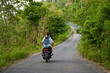 A person on a motorcycle rides a scenic asphalt road in Asia.